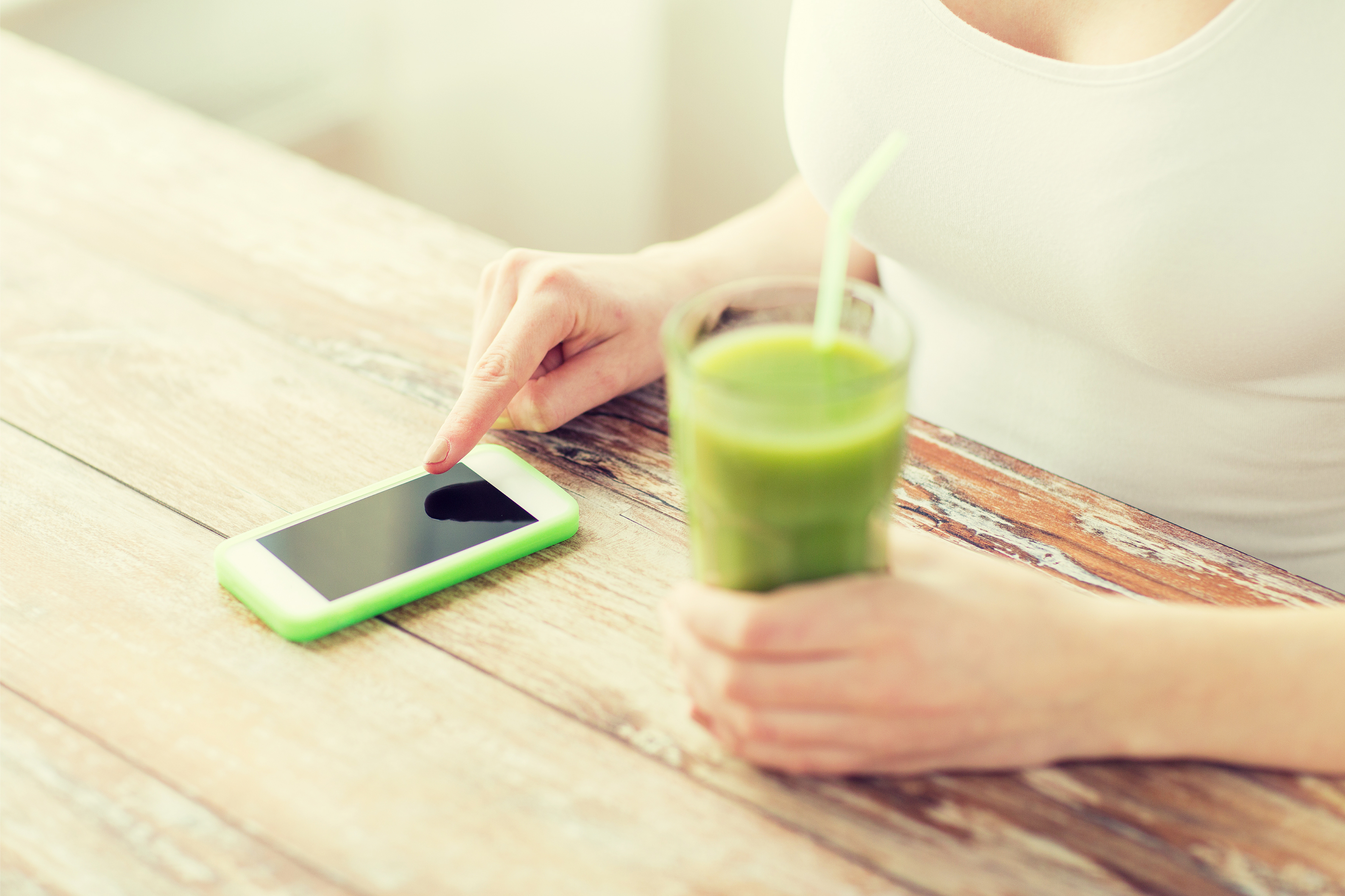 Close up of a womans hands on a table with a smartphone and a green smoothie, taking part in market research for the media industry