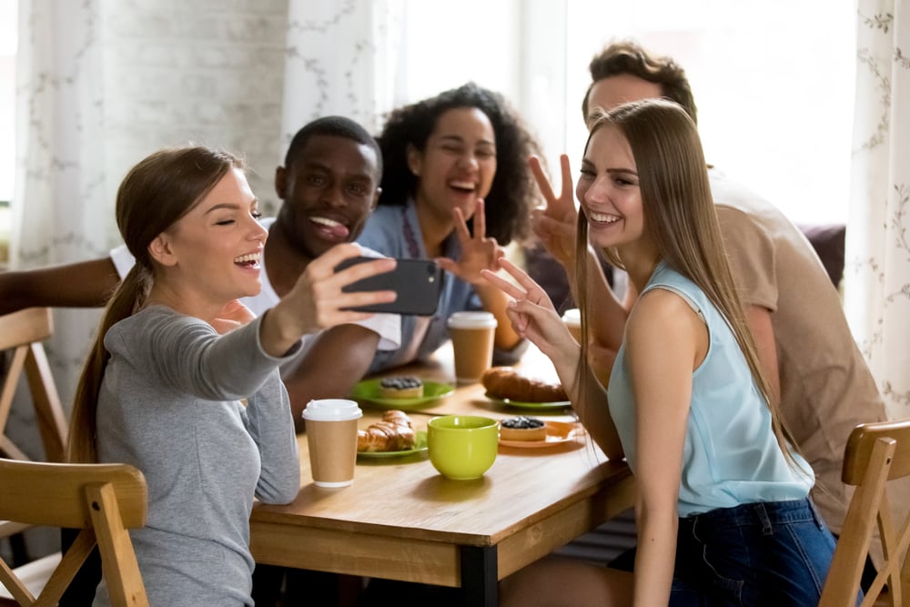 A group of young people in a cafe taking a selfie as part of a market research insight and data gathering project