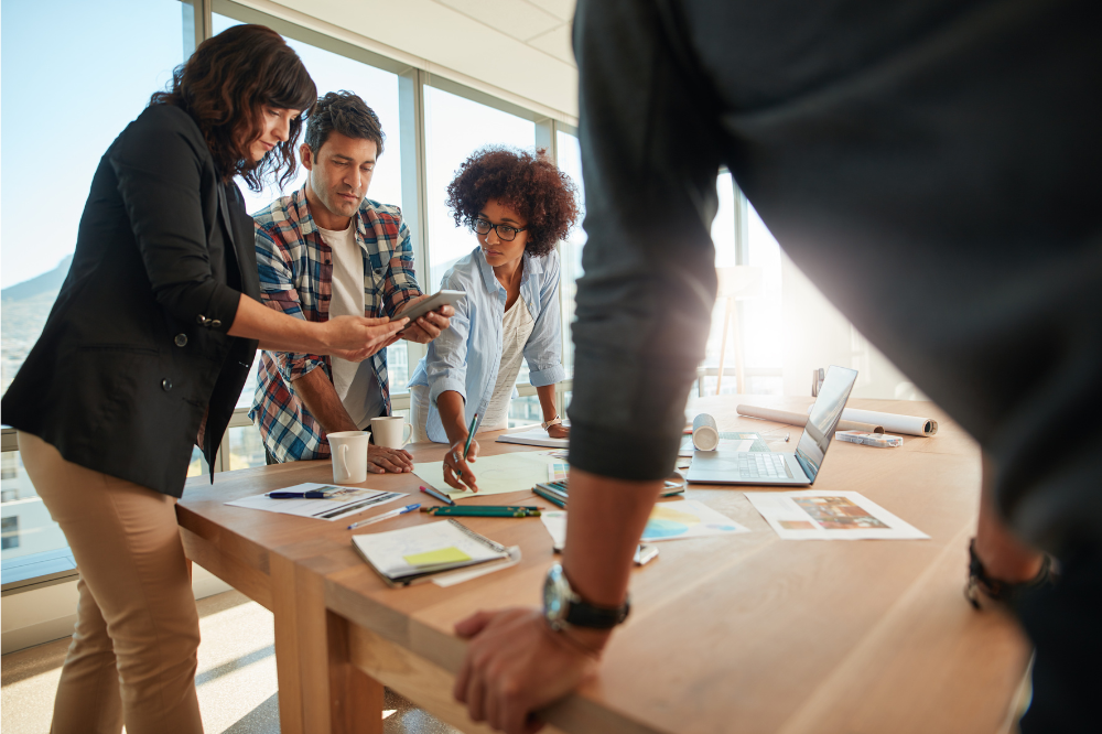 4 people standing around a table planning to run a pilot study for qualitative market research