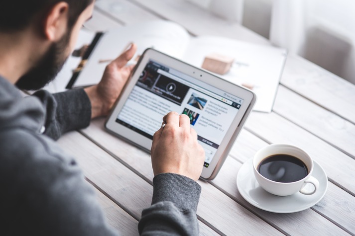 Man looking at newsfeed on tablet with a cup of coffee as part of Gen Z qualitative market research